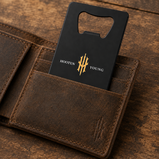 Black bottle opener with gold logo in a brown leather wallet on a wooden surface